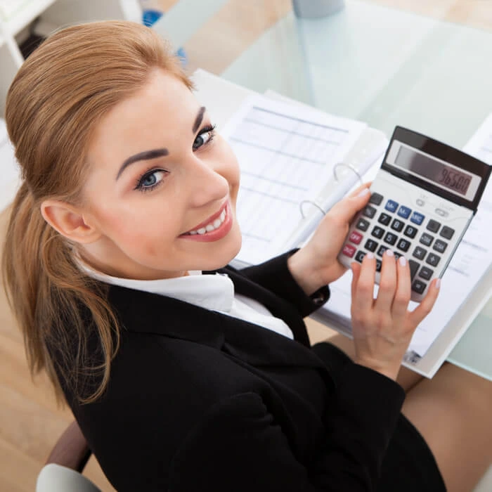 Smiling female accountant working on financial documents and using a calculator at her desk